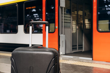 Black suitcase with wheels positioned on platform, train approaching in background, showcasing...