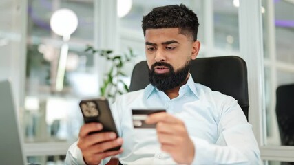 Professional bearded man in a light blue shirt intently uses a smartphone and credit card for secure online banking or shopping in a modern office, showing concentration. - Powered by Adobe