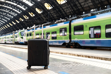 Black suitcase with wheels positioned on platform, train approaching in background, showcasing...