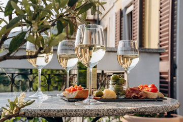 Outdoor dining or aperitif white wine glasses on a stone table with gourmet charcuterie board assorted meats, olives, and cheese