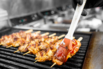 Close-up of a gloved hand brushing barbecue sauce onto grilled chicken skewers, highlighting juicy...