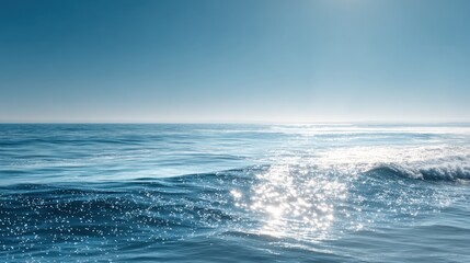 Serene ocean waves with sparkling water surface under clear blue sky during daytime.