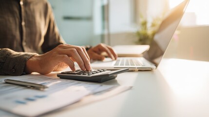 Fototapeta premium Person Using Calculator and Laptop at Desk in Bright Office Workspace.