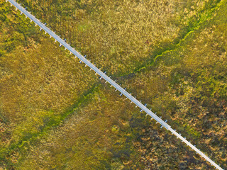 Abstract top-down drone view of a straight wooden boardwalk diagonally crossing the textured...