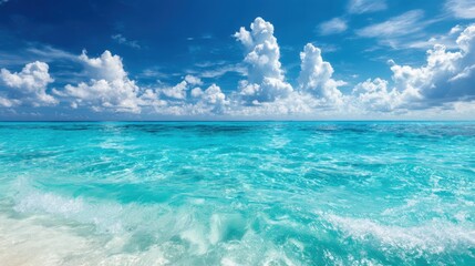 Fototapeta premium Stunning turquoise ocean waves crashing onto sandy shore under bright blue sky with fluffy clouds.