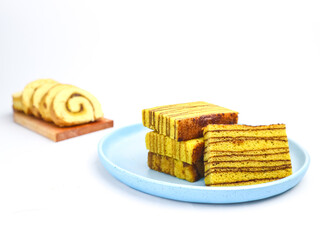 Layered Indonesian cake (lapis legit) served on a blue plate, with sliced sponge roll in the background