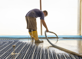 Man pouring concrete over floor heating installation in a new building. Modern construction system