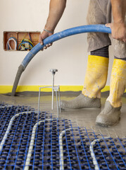 Man pouring concrete over floor heating installation in a new building. Modern construction system