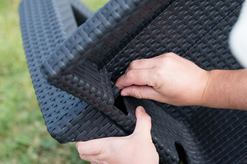 Assembling outdoor patio furniture. Hands connect woven plastic pieces.