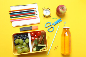 lunchbox with snacks, fruits, vegetables and water, as well as school supplies on a yellow background