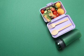 Lunchbox with snacks, fruits, vegetables and water, as well as school supplies on a green background