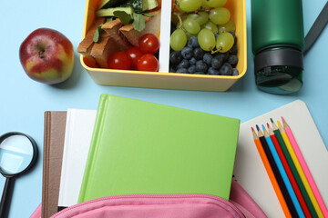 healthy lunch box with school backpack, apple and stationery on color background
