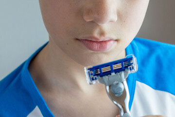 Nervous teen boy hesitates with razor in hand, symbolizing awkward transition into manhood,...