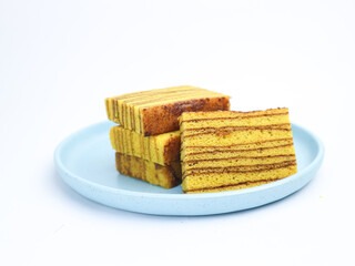 Slices of layered Indonesian lapis legit cake neatly stacked on a light blue plate, isolated on white background.