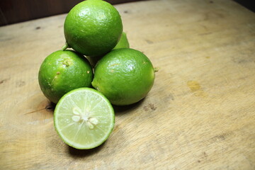 Stacked of fresh green limes on a rustic wooden surface, with two halves showing the juicy, citrus...
