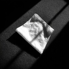 Folded white cloth on dark floor, sunlit shadows