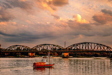 Obraz premium old wooden boat on the river, beauty clouds, sunset, bridge, beautiful view