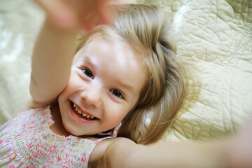 A small child with blond hair lies on the bed. Baby girl is playing on the couch.