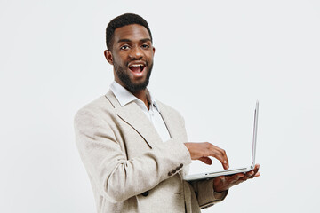 Smiling young man with African descent holding a laptop computer in hand, wearing a beige blazer...