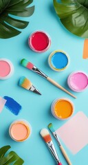 Vibrant paint containers and brushes arranged on a light-blue surface, surrounded by tropical leaves and paint swatches
