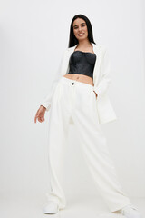 Smiling woman standing confidently in white wide-leg pants and blazer with black leather cropped...