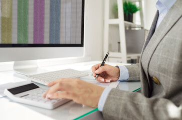 Focused businesswoman calculating expenses and taking notes while reviewing financial spreadsheet...