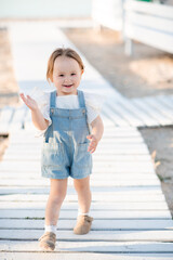 Smiling baby girl 2-3 year old wearing denim dress at beach. Summer vacation season. Childhood.