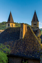 Twin spires and ancient tiled roofs and historic towers of the Abbey of Sainte-Foy, in the medieval village of Conques, France, illuminated by the golden light of sunset.