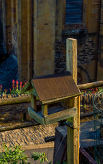 A wooden birdhouse illuminated by the sunset light in a rustic village garden with a stone church in the background.