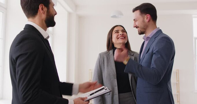 Man realtor handing over house keys to young married couple who have bought new house or flat, being very happy to buy property, having talk with salesman. Family homeowners in apartment