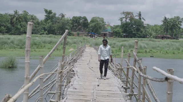 A man stands on the bamboo bridge built over the Damodar River and enjoys the natural beauty.