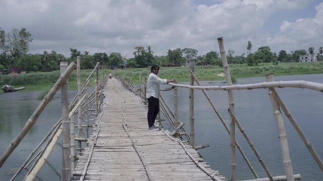 A man stands on the bamboo bridge built over the Damodar River and enjoys the natural beauty.