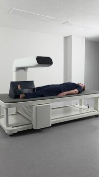 Wide shot of a male patient lying on a modern DEXA scanner table, undergoing a full-body scan for bone density measurement and body composition analysis in a hospital.