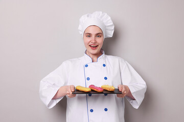 Confectioner in uniform holding delicious eclairs on light grey background