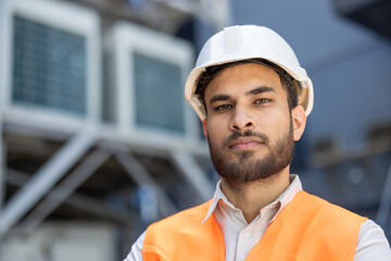 A construction worker, wearing a hard hat and safety vest, looks directly at the camera with a...