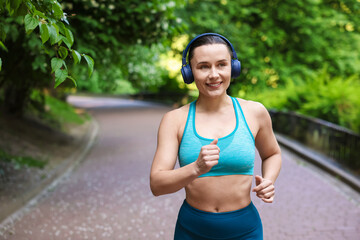Sporty woman with headphones running in park, space for text