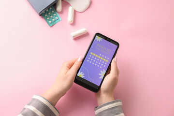 Menstruation. Woman holding smartphone with period calendar application on pink background, top view