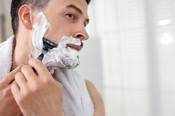 Handsome man shaving with razor at home. Space for text