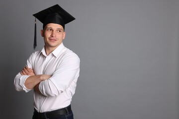 Happy student with crossed arms after graduation on grey background. Space for text