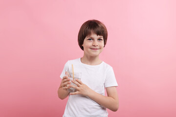 Cute little boy with glass of refreshing soda drink on pink background