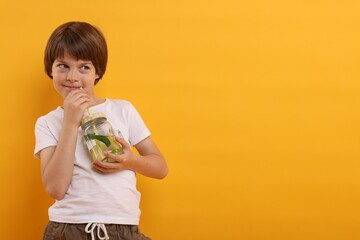 Cute little boy drinking lemonade on orange background, space for text. Refreshing drink