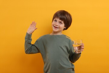 Cute little boy with glass of refreshing soda drink on orange background