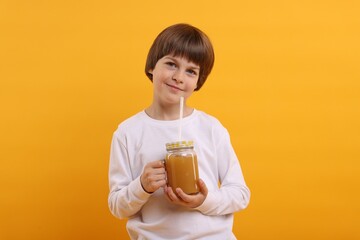 Cute little boy with mason jar of juice on orange background. Refreshing drink