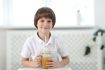 Little boy with mason jar of orange juice at table indoors. Refreshing drink