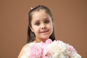 Cute little girl with bouquet of beautiful peonies on brown background