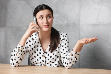Young businesswoman complaining to someone via phone at wooden table indoors
