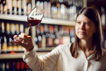 Profesional female bartender rates red wine, looks at its color, evaluates the density and tartness...
