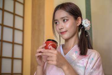 Portrait young attractive Japanese woman in traditional kimono or yukata cloth holding tea cup in...