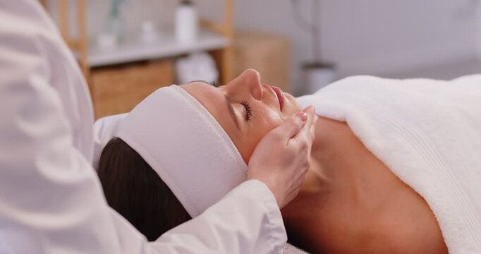 Relaxed young woman enjoying face building massage, visiting professional therapist, undergoing beauty treatments, has anti aging session, keeping eyes closed, having relaxing therapy