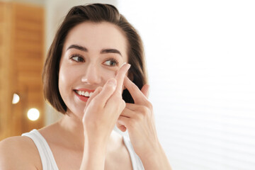 Beautiful woman putting in contact lens indoors. Space for text